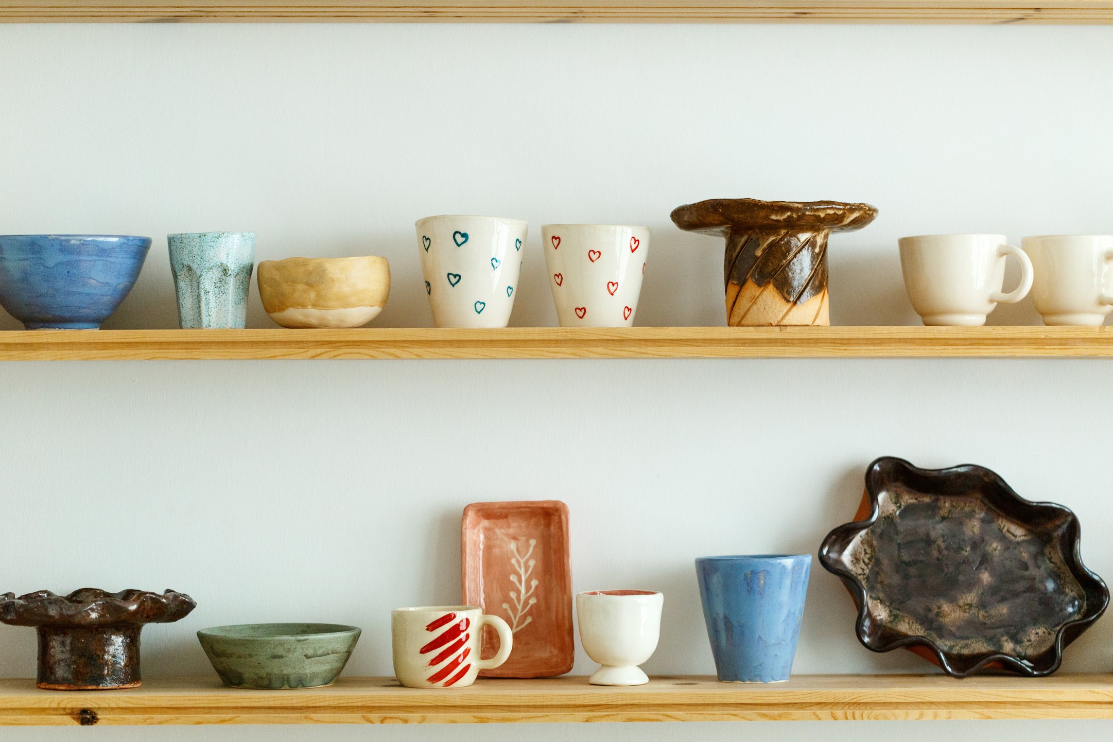 Handmade ceramic crockery and craft pottery jug, jars and cups standing on shelves in creative studio or potter store. Different handicraft clay earthenware bowls in artisan craftsman classes workshop